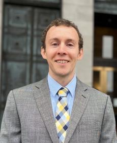 Headshot of Beau Perschbacher, a man with a grey jacket and a blue shirt